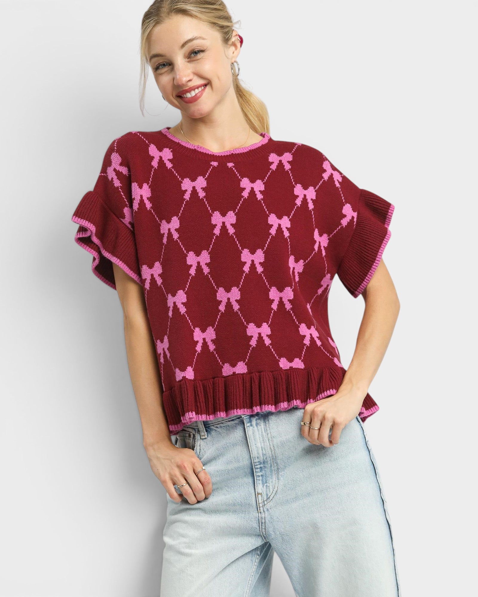 Woman wearing a maroon sweater with pink bow pattern against a white background