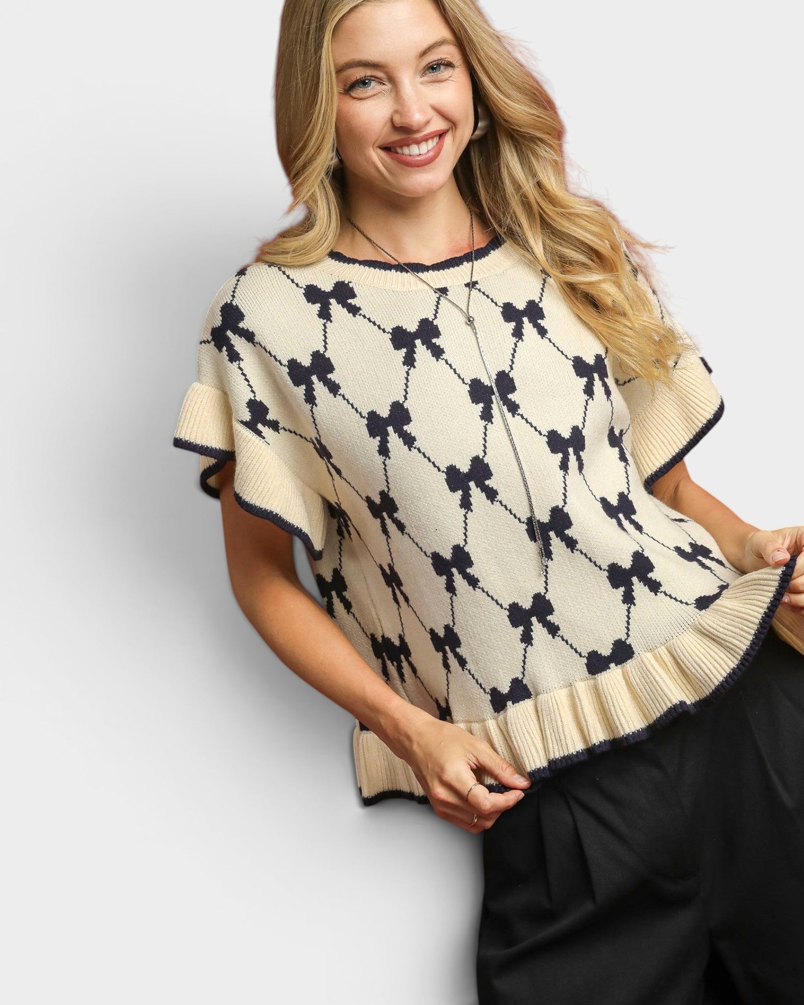 Woman wearing a cream-colored sweater with black bow pattern on a white background