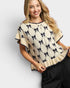 Woman wearing a cream-colored sweater with black bow pattern on a white background
