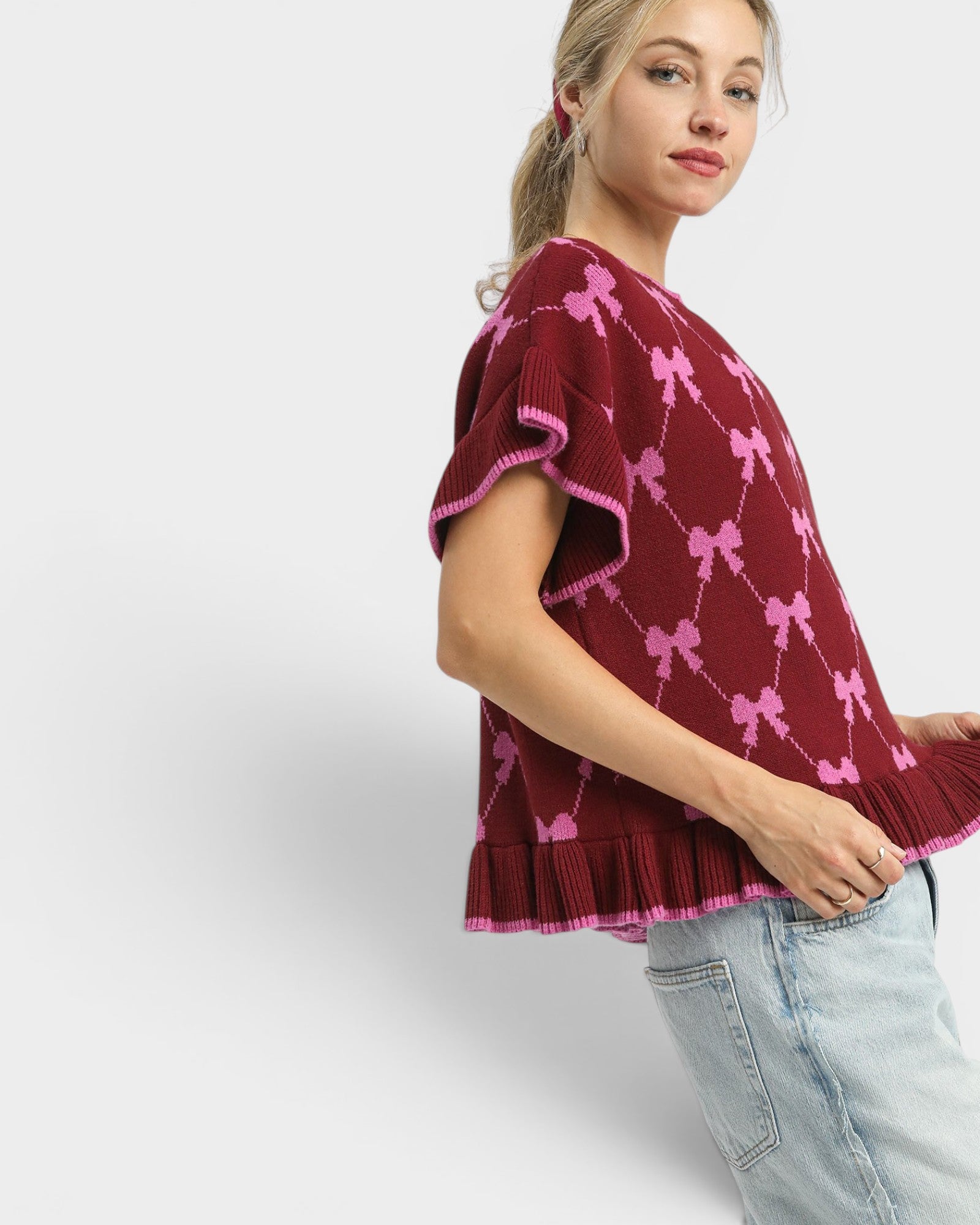 Woman wearing a burgundy poncho with pink bow patterns on a white background