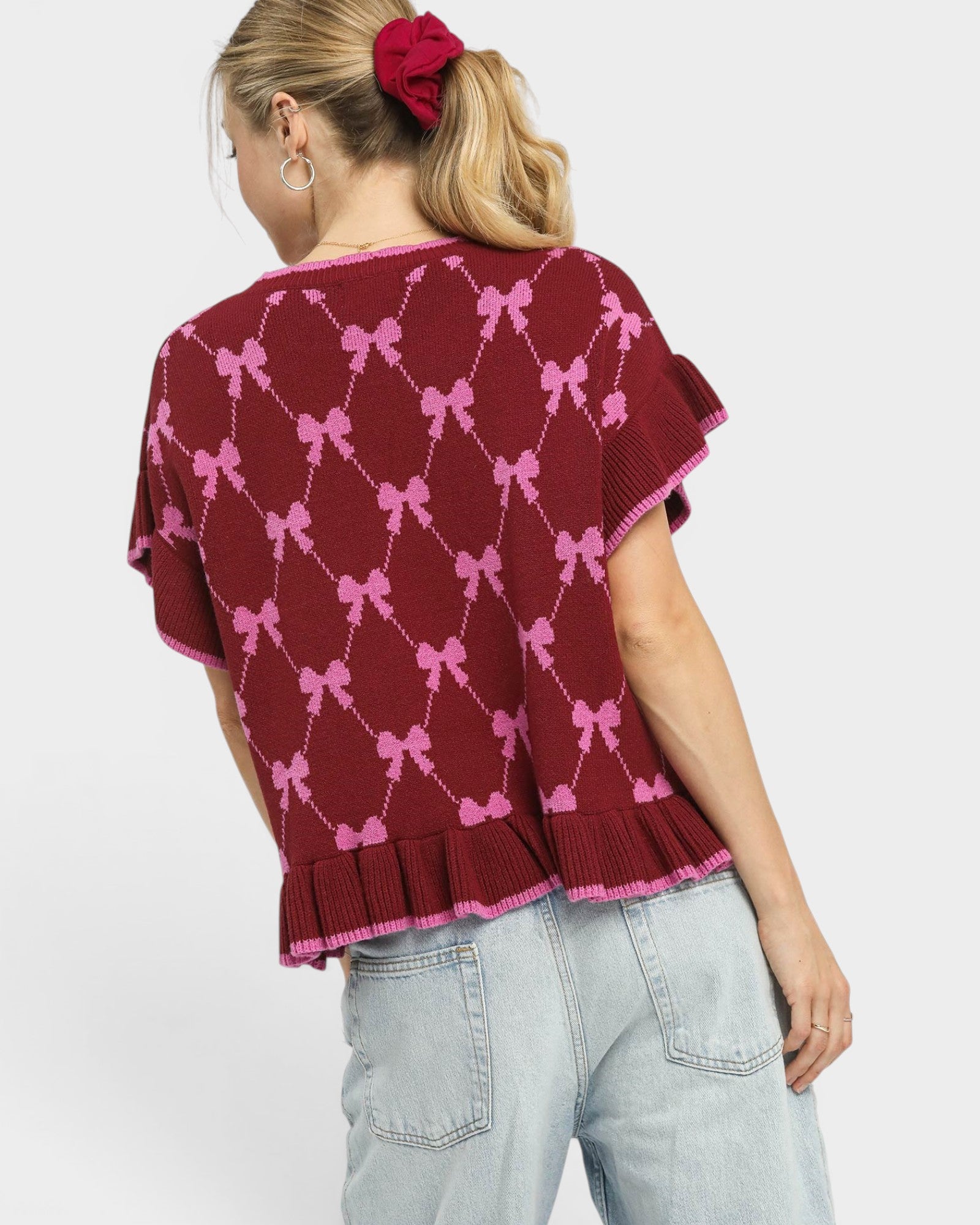 Woman wearing a maroon sweater with pink bow pattern on a plain background