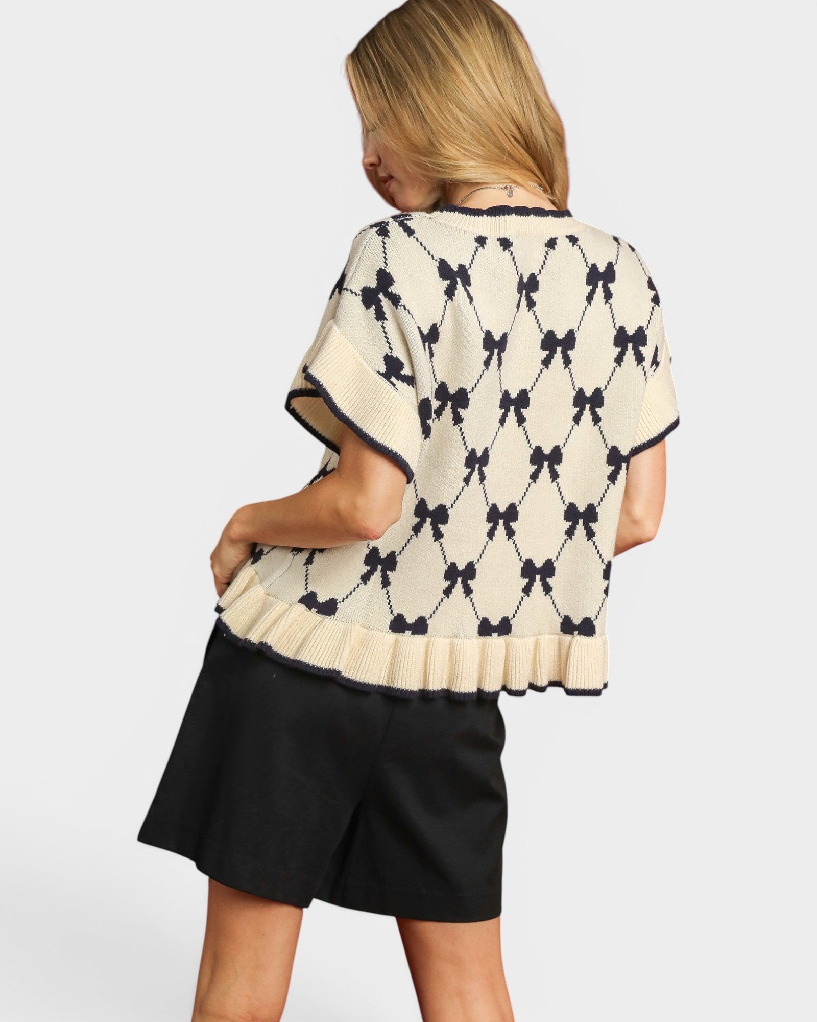 Woman wearing a cream-colored sweater with black bow pattern and black shorts on a white background