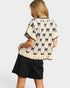 Woman wearing a cream-colored sweater with black bow pattern and black shorts on a white background