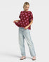 Woman wearing a burgundy sweater with pink bow pattern and light blue jeans on a white background