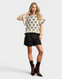 Woman wearing a patterned top and black shorts on a white background