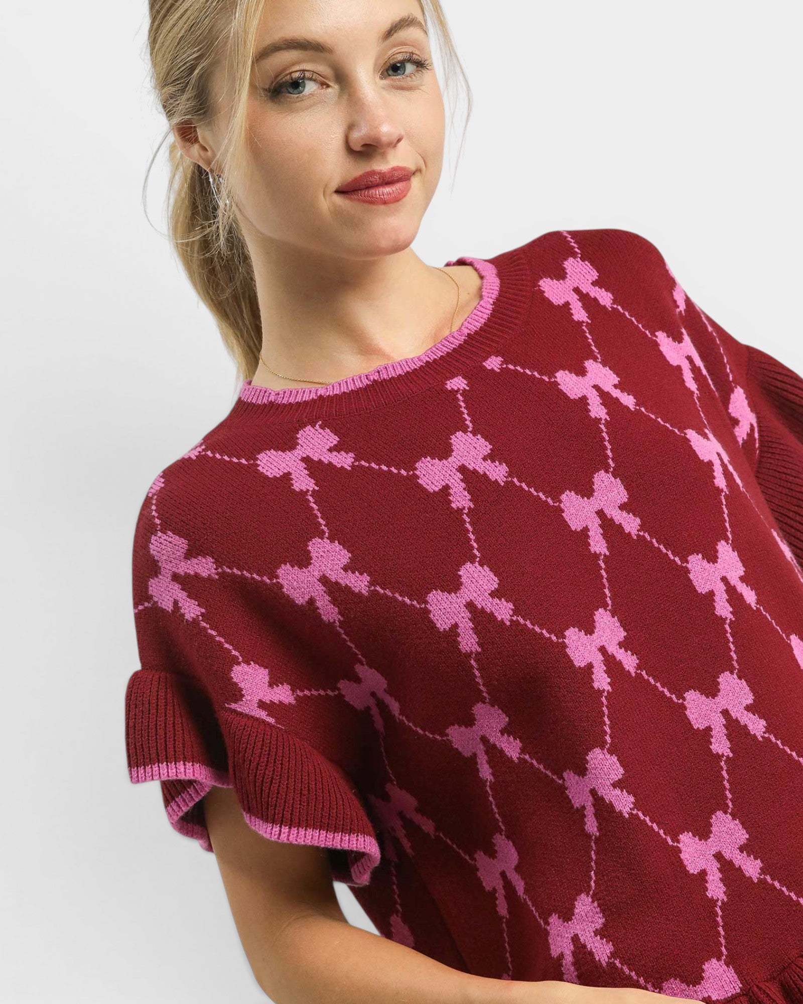Woman wearing a maroon sweater with pink bow pattern on a white background
