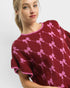 Woman wearing a maroon sweater with pink bow pattern on a white background