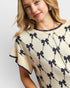 Woman wearing a beige sweater with black bow pattern on a plain background