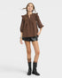 Woman wearing a brown blouse with ruffled sleeves and black leather shorts on a white background