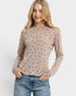Woman wearing a patterned long-sleeve top and jeans on a plain background