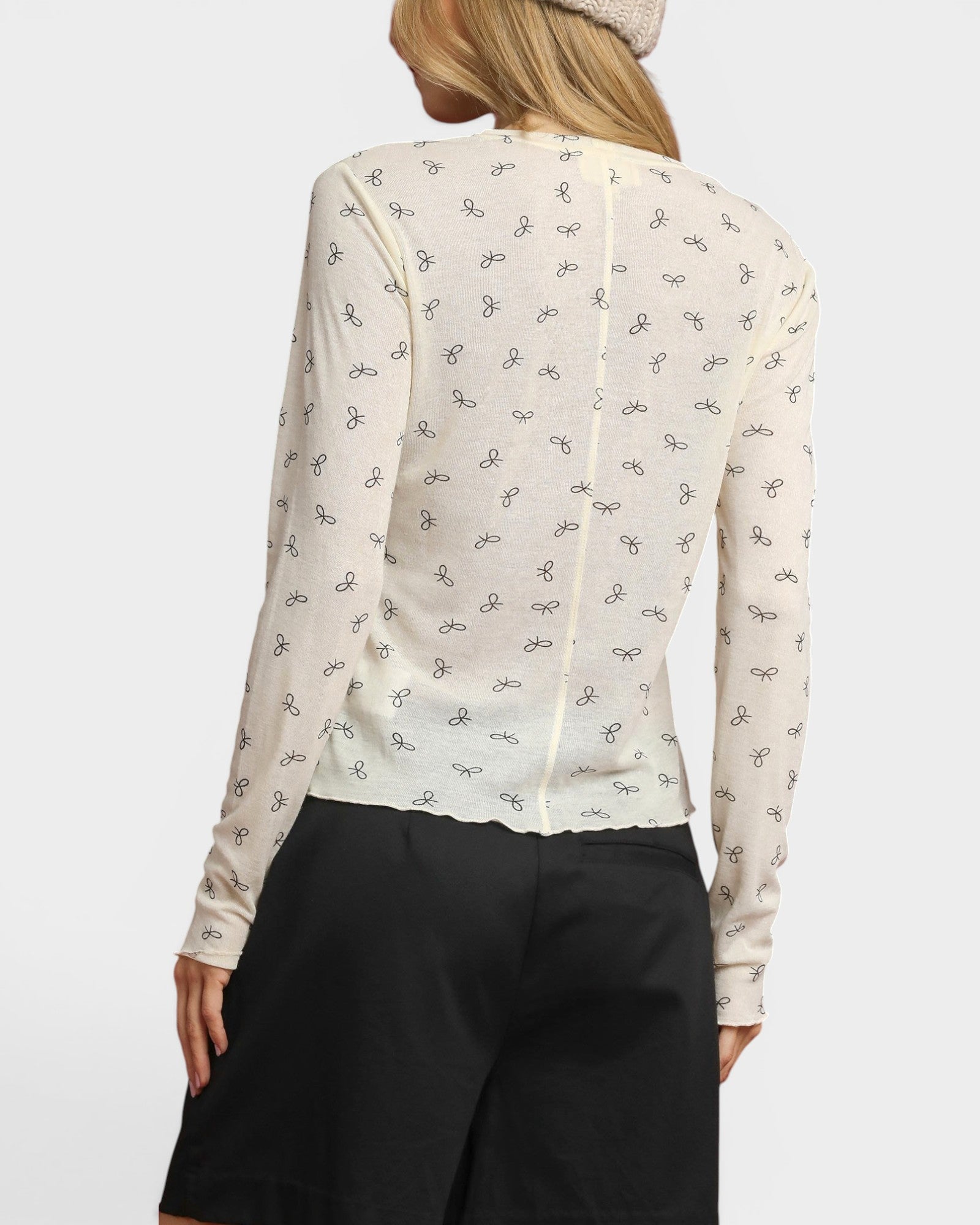 Person wearing a white blouse with black patterns and black pants on a white background