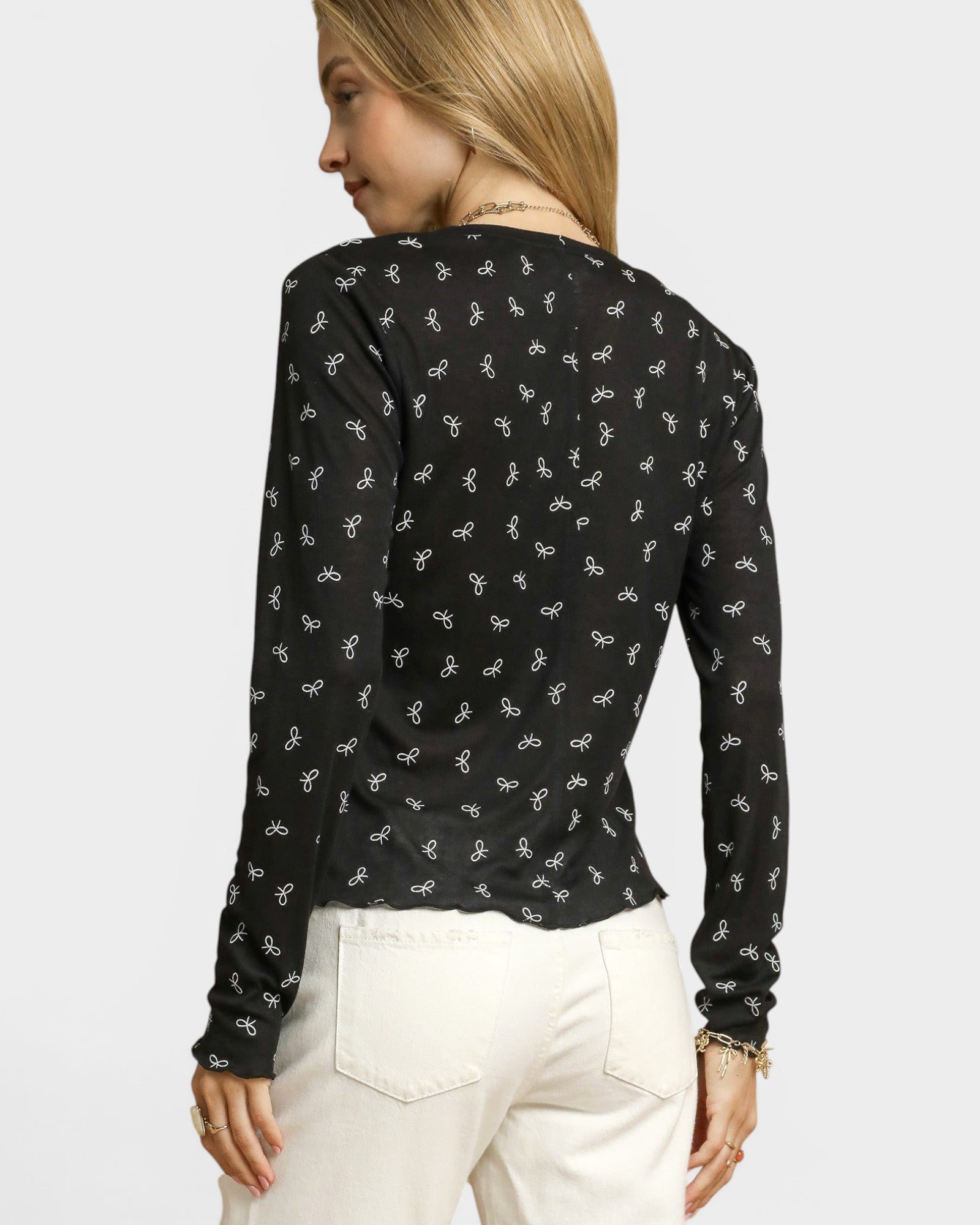 Woman wearing a black long-sleeve top with white patterns on a plain background