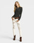 Woman wearing a black patterned top, white distressed jeans, and brown boots on a white background
