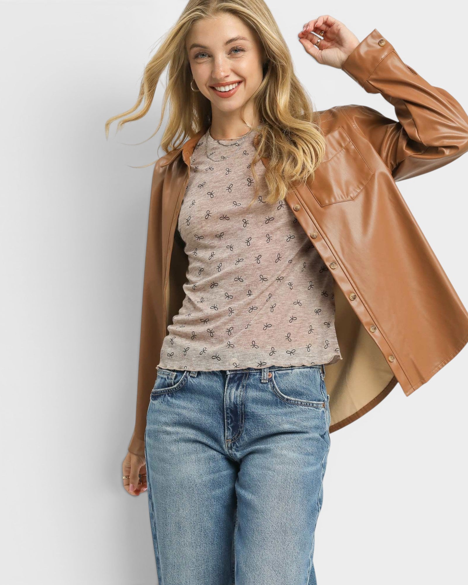 Woman wearing a brown leather jacket, floral top, and blue jeans on a light gray background