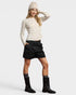 Woman wearing a cream sweater, black skirt, and black boots on a white background