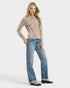 Woman wearing a patterned long-sleeve top and blue jeans on a white background