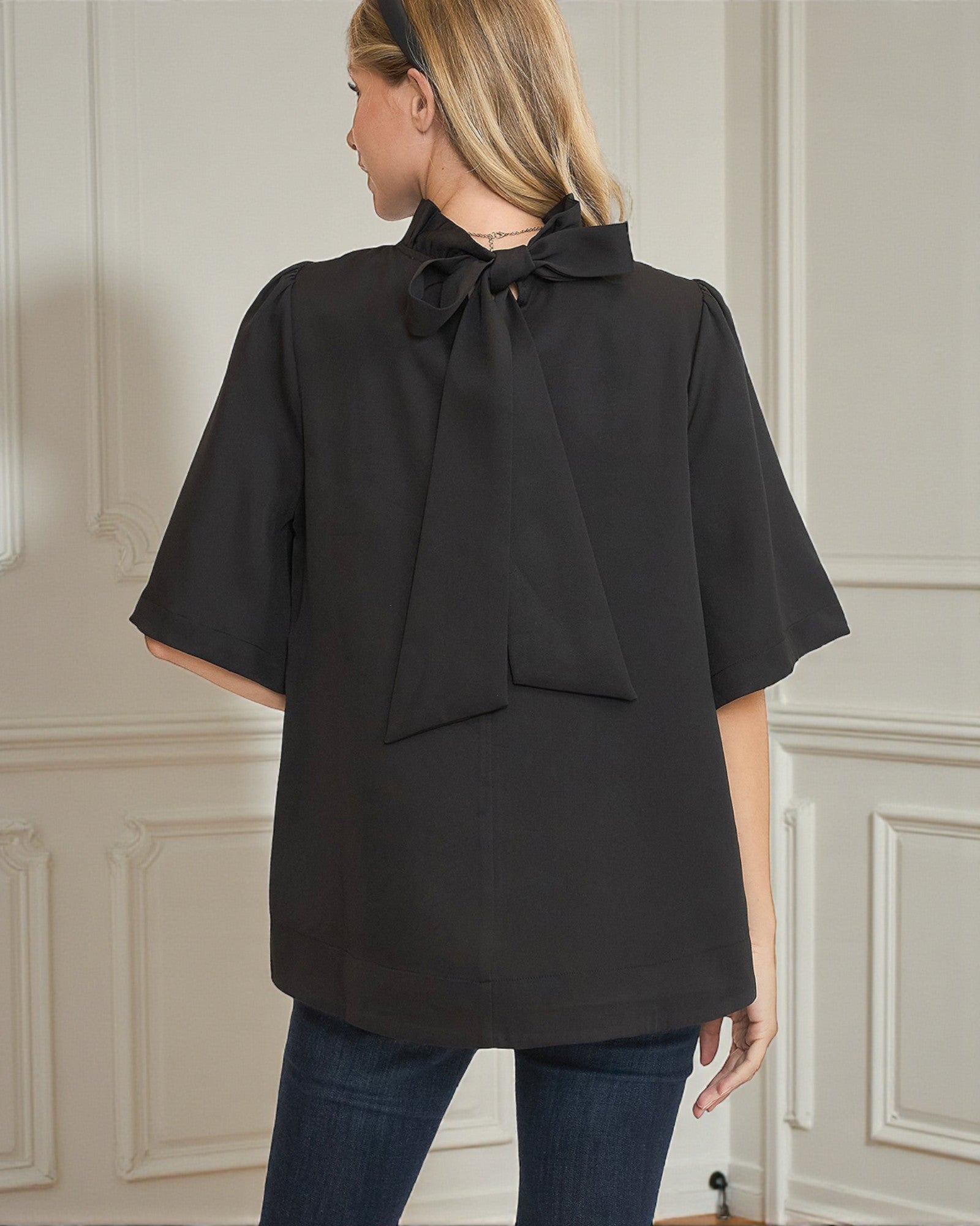 Woman wearing a black blouse with a bow detail on a neutral background