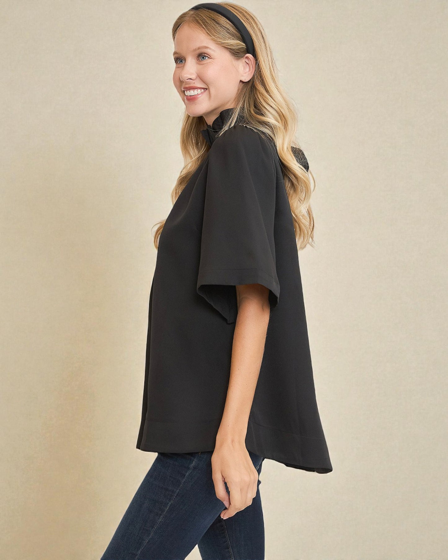 Woman wearing a black top and blue jeans against a beige background