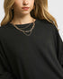 Person wearing a black sweater with layered gold necklaces on a plain background