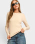 Woman wearing a beige ribbed sweater and blue jeans on a light gray background