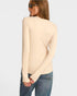 Woman wearing a beige ribbed sweater and blue jeans on a light gray background