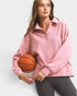 Woman holding a basketball wearing a pink pullover on a white background