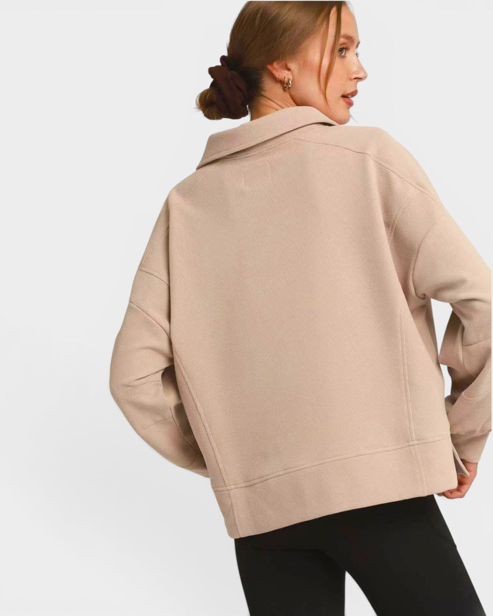 Woman wearing a beige pullover with a plain background