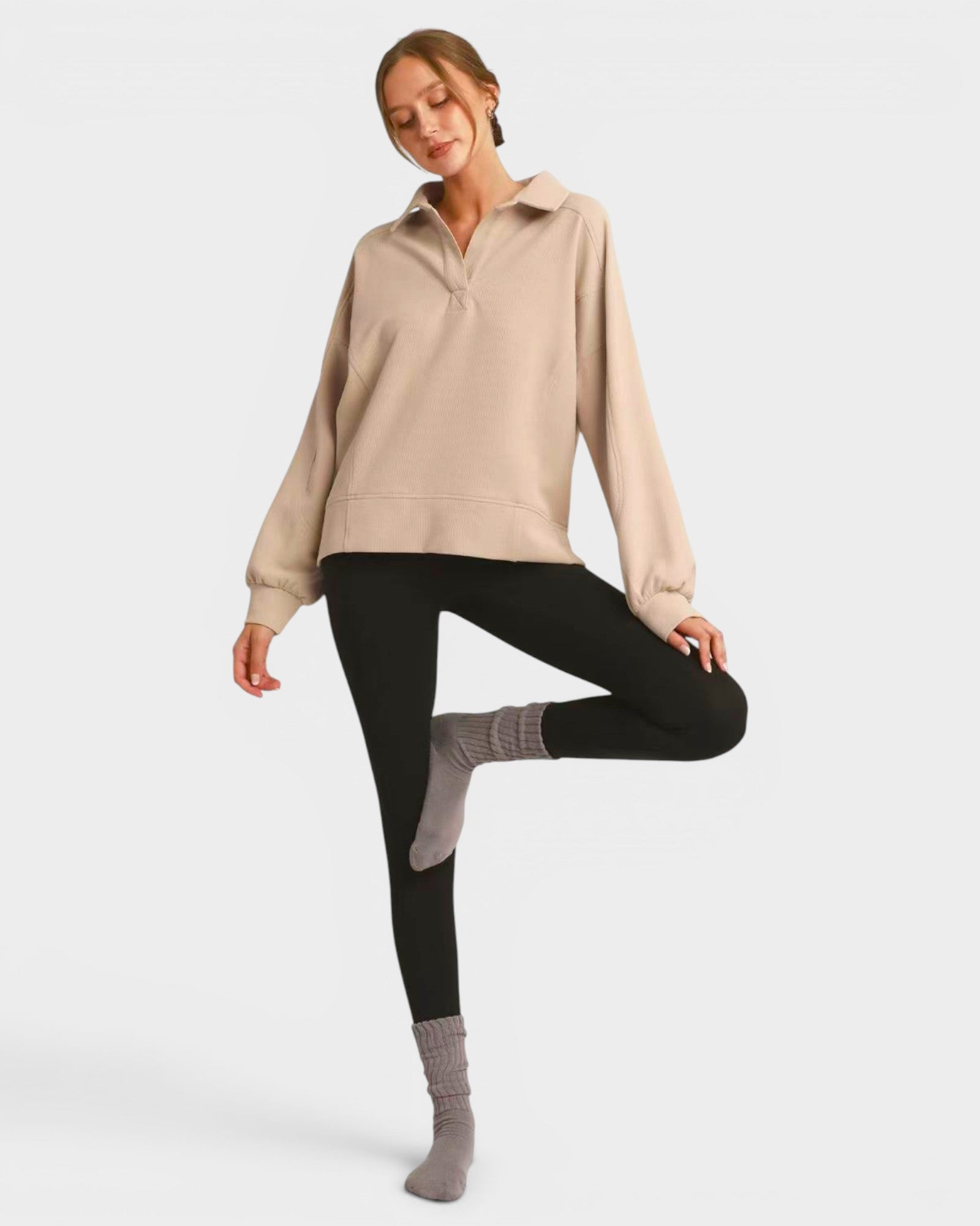 Woman wearing a beige sweater and black leggings on a white background