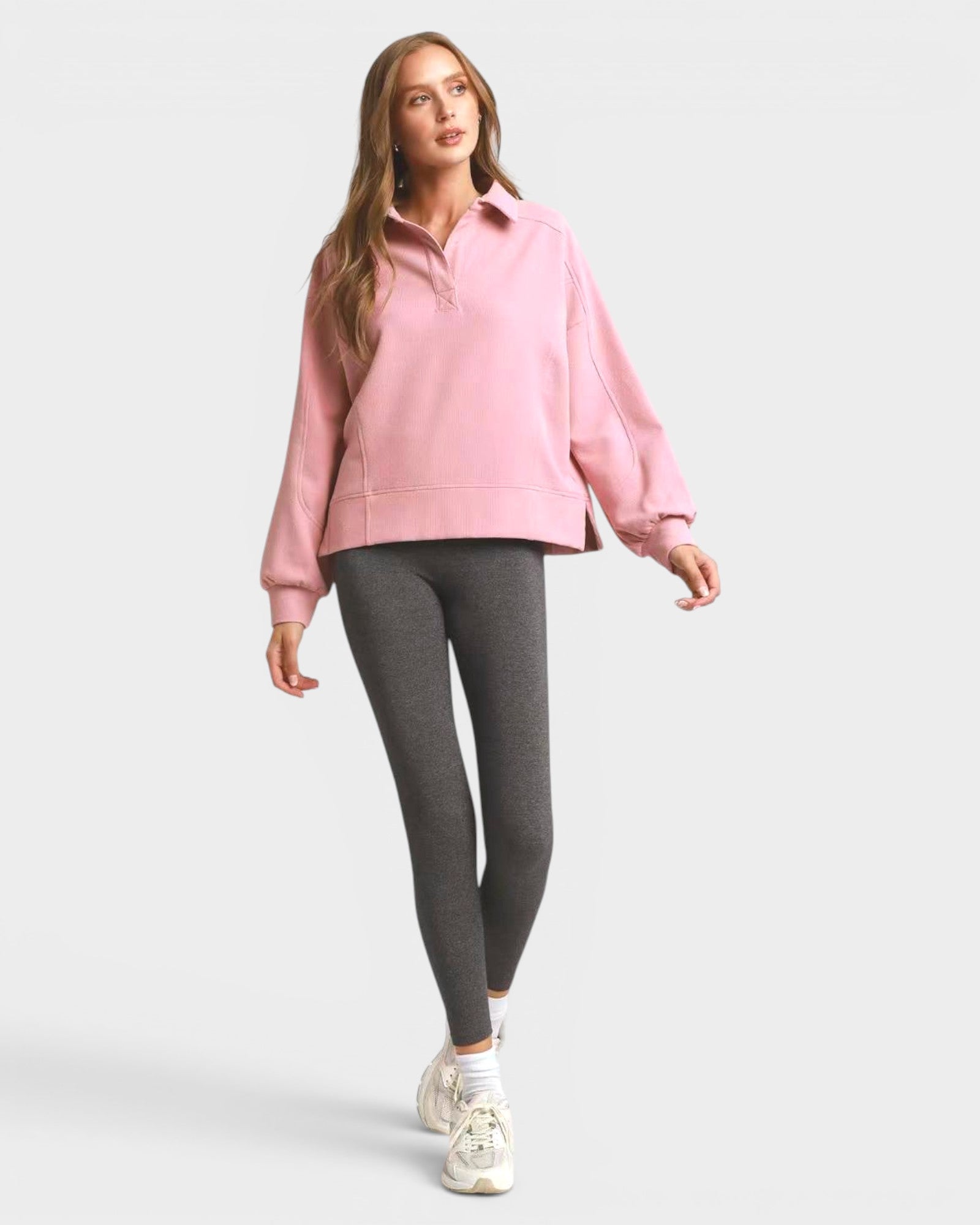 Woman wearing a pink sweatshirt and gray leggings on a white background