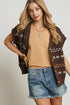 Woman wearing a brown patterned vest over a beige top and denim shorts on a plain background