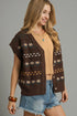 Woman wearing a brown patterned cardigan over a beige top and denim shorts on a gray background
