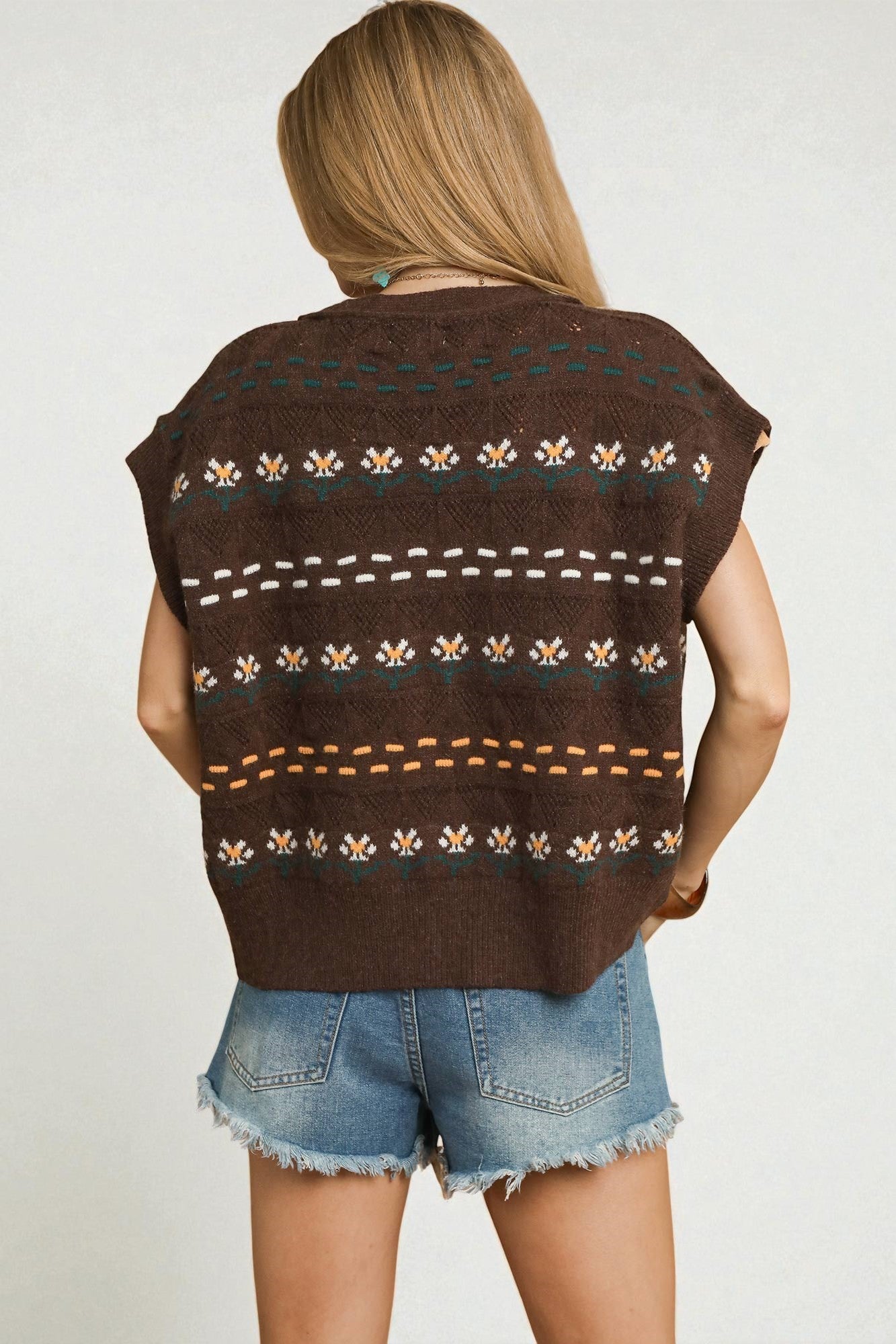 Person wearing a brown patterned sleeveless top with denim shorts on a plain background