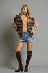 Woman wearing a brown vest, beige top, denim shorts, and brown knee-high boots on a gray background