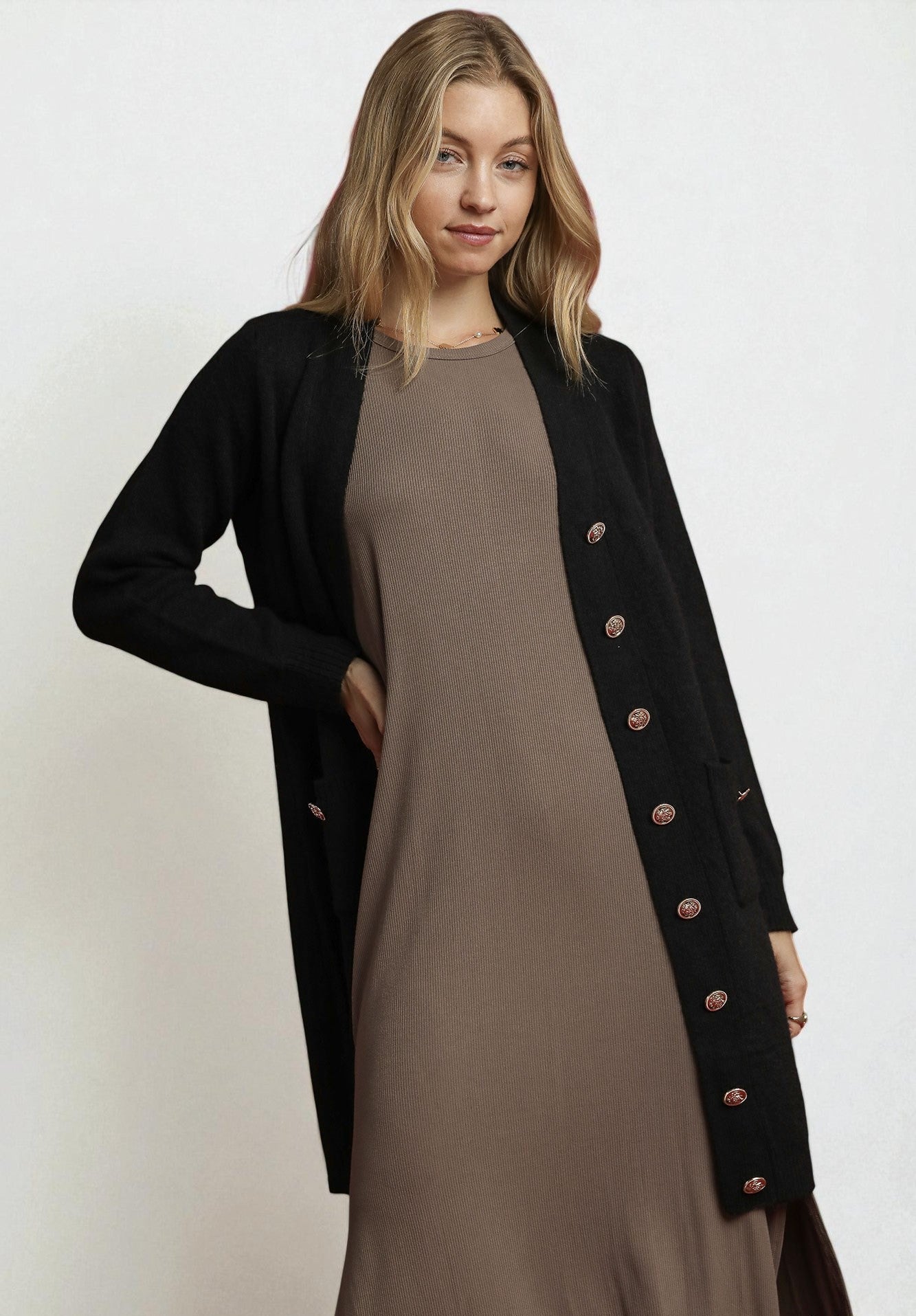 Woman wearing a long black cardigan with button details over a brown dress on a white background