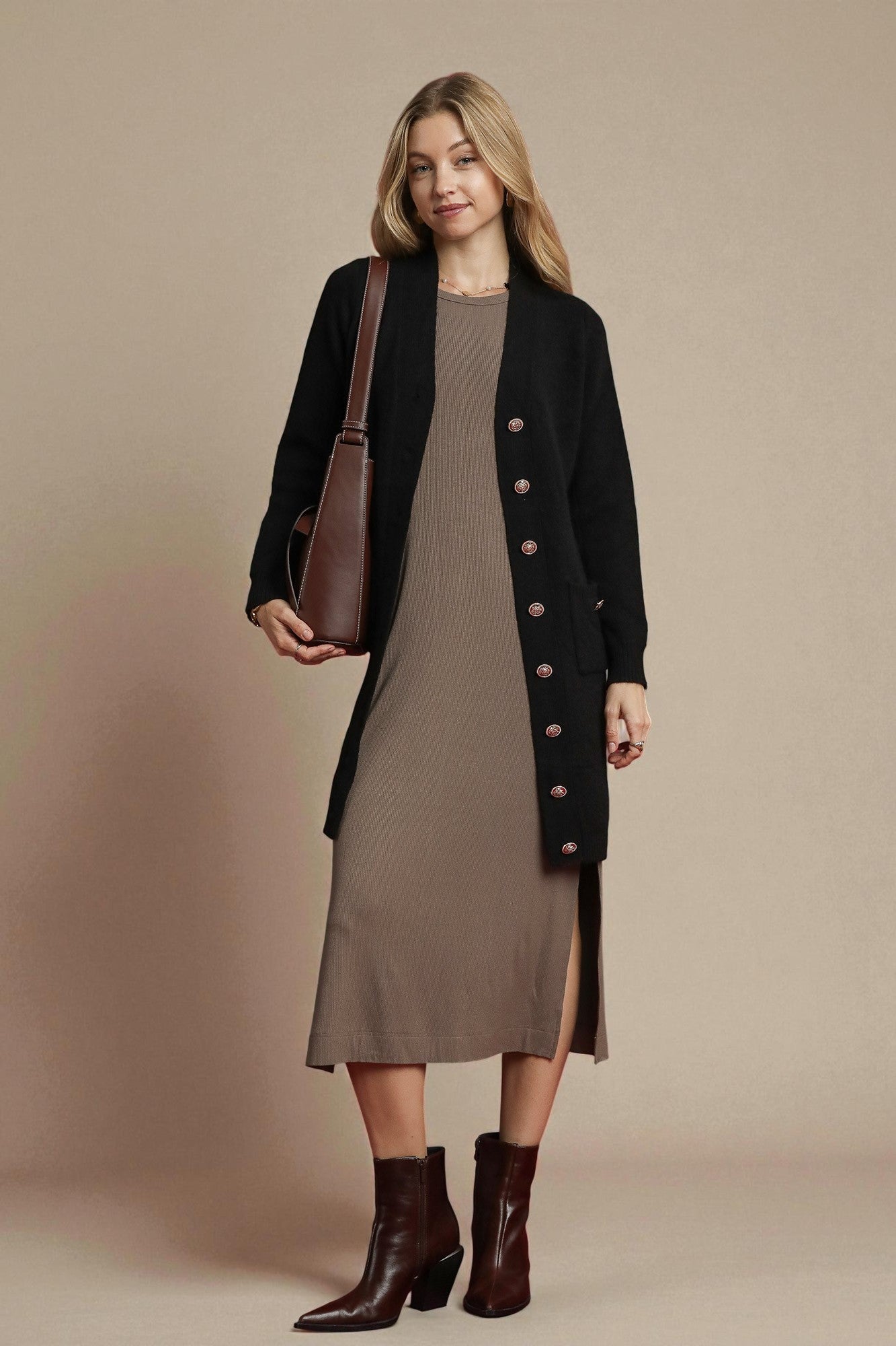 Woman wearing a black cardigan over a brown dress with a brown bag on a beige background