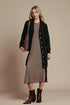 Woman wearing a black cardigan over a brown dress with a brown bag on a beige background