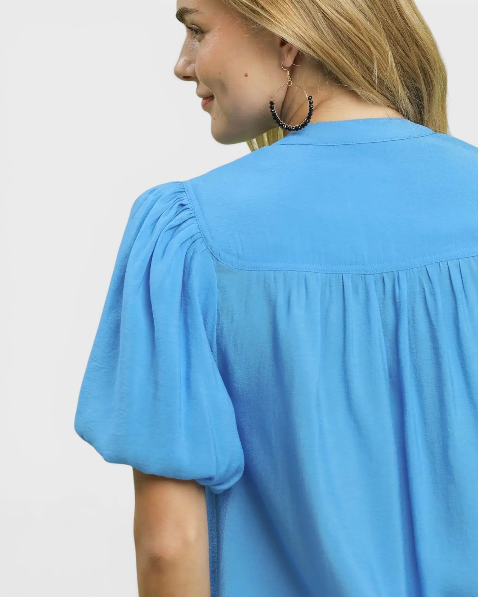 Woman wearing a blue blouse with puffed sleeves on a plain background