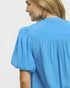 Woman wearing a blue blouse with puffed sleeves on a plain background
