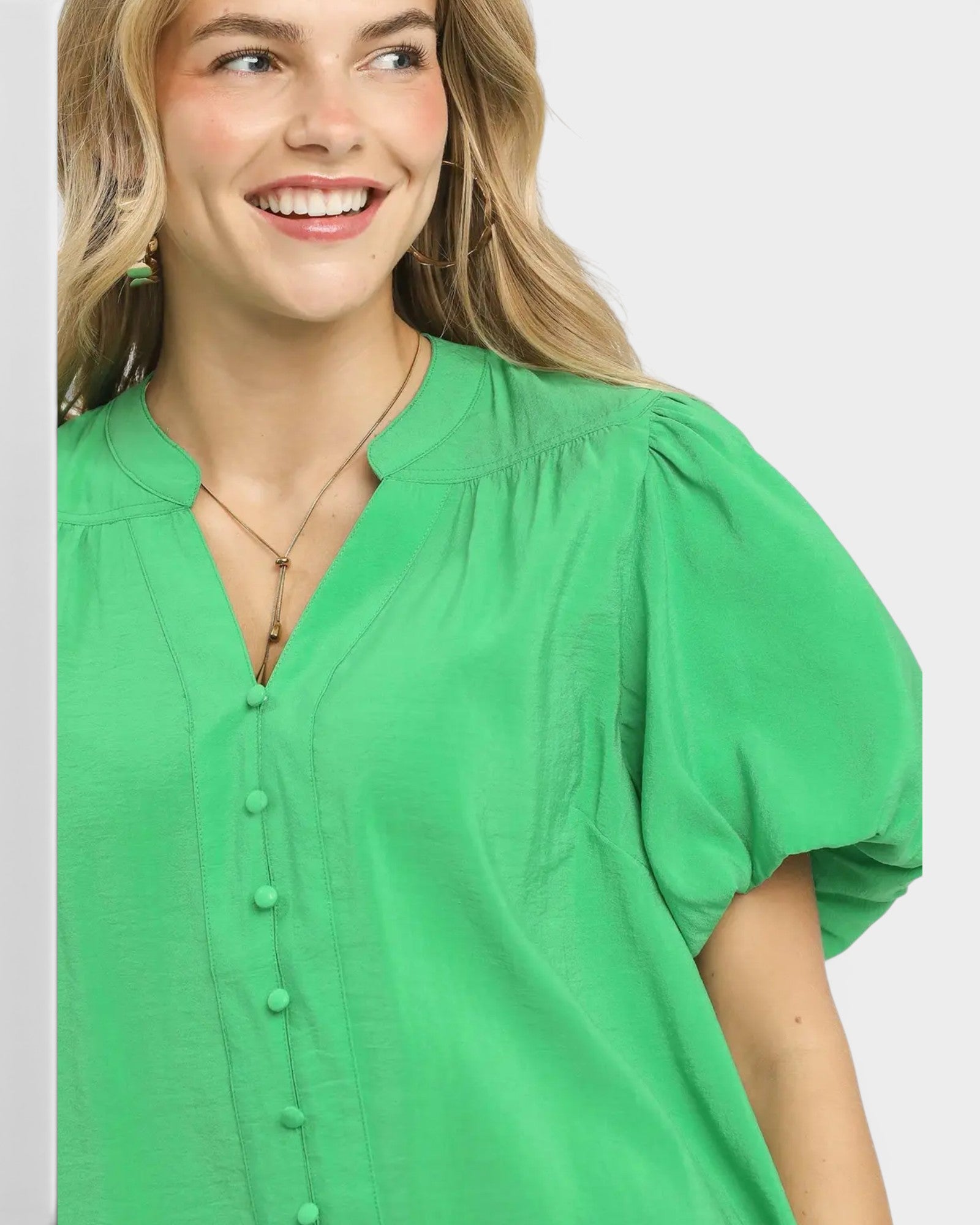 Woman wearing a green blouse with puff sleeves on a plain background