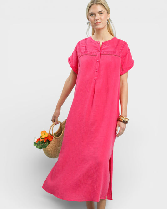 Woman wearing a bright pink dress holding a woven bag with flowers on a white background