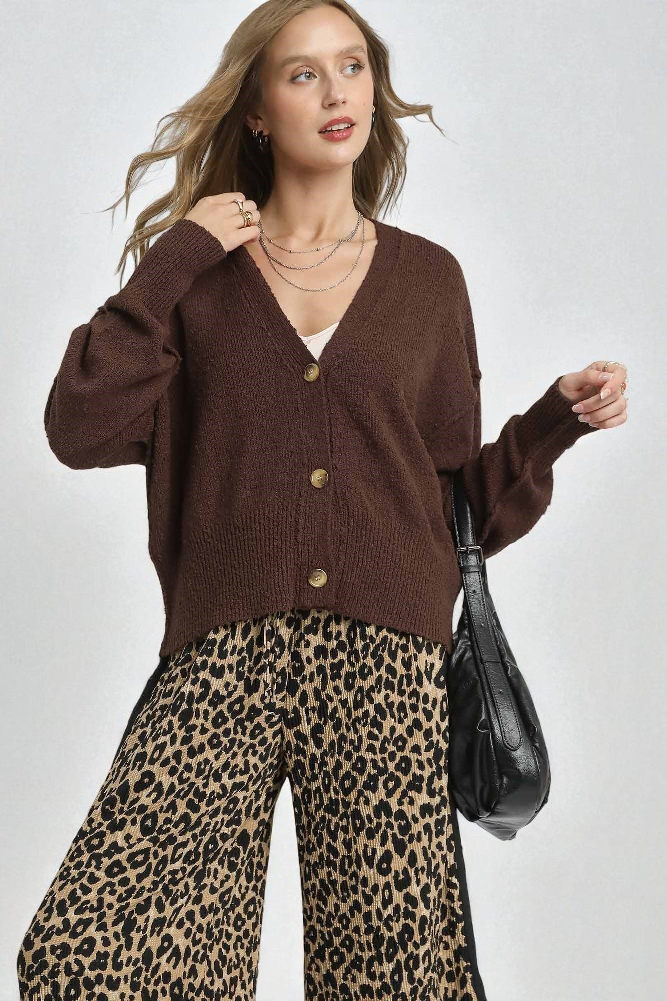 Woman wearing a brown cardigan and leopard print pants with a black handbag on a white background