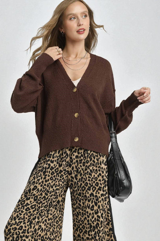 Woman wearing a brown cardigan and leopard print pants with a black handbag on a white background