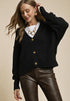 Woman wearing a black cardigan with gold buttons and brown leather pants on a beige background