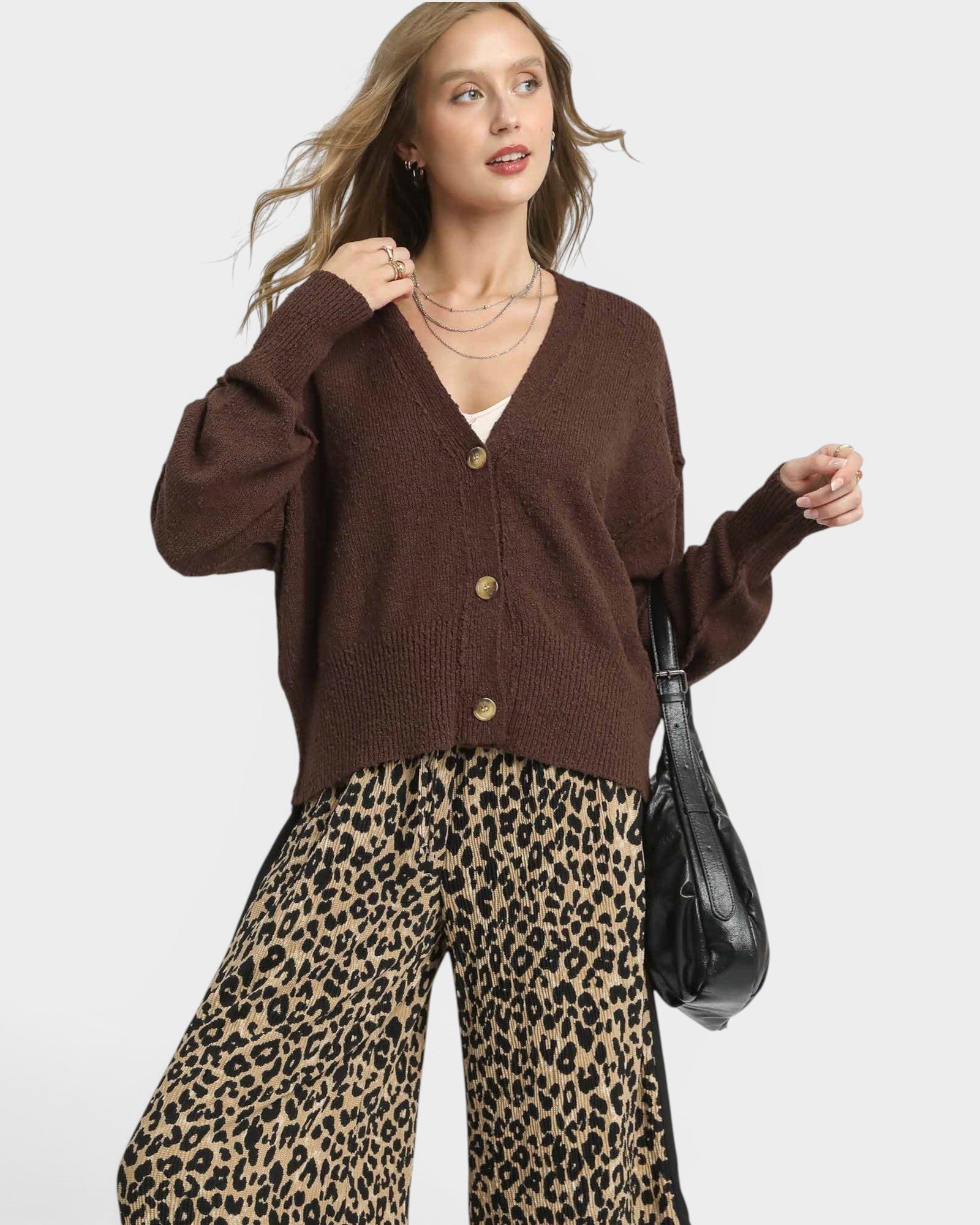 Woman wearing a brown cardigan and leopard print pants on a white background