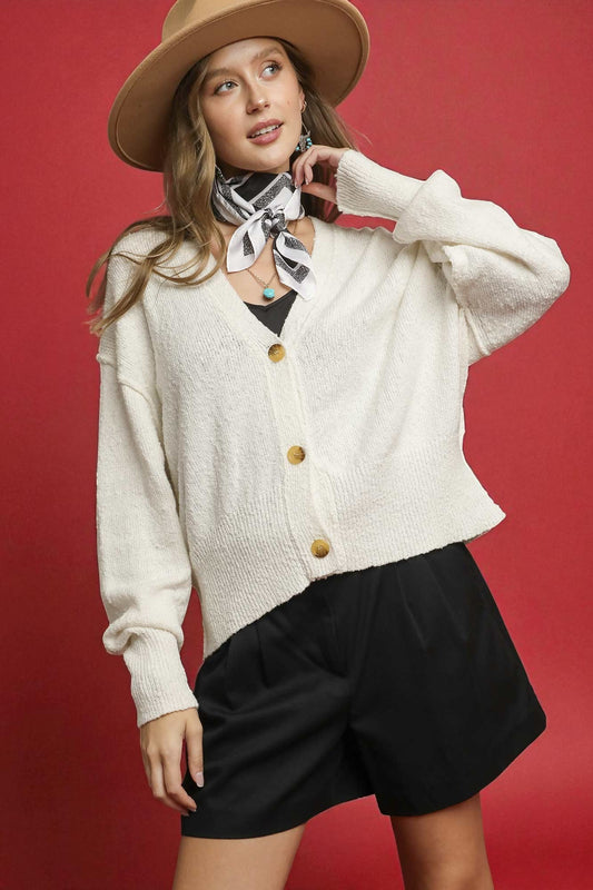 Woman wearing a beige cardigan, black shorts, and a beige hat against a red background