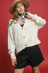 Woman wearing a beige cardigan, black shorts, and a beige hat against a red background