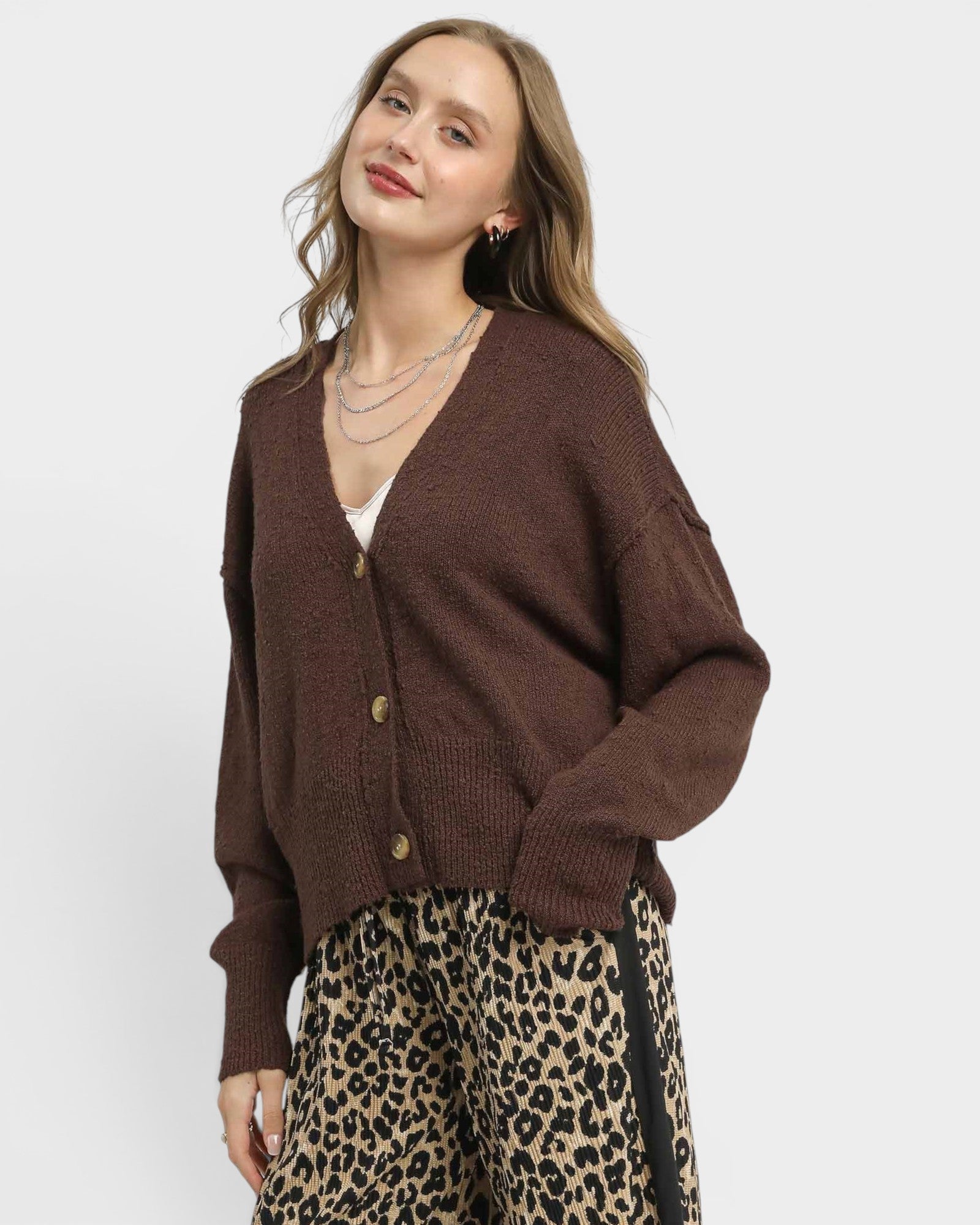Woman wearing a brown cardigan and leopard print pants on a white background