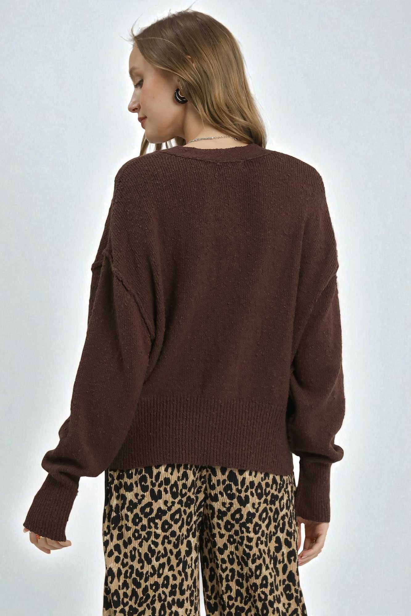 Woman wearing a brown sweater and leopard print pants on a white background