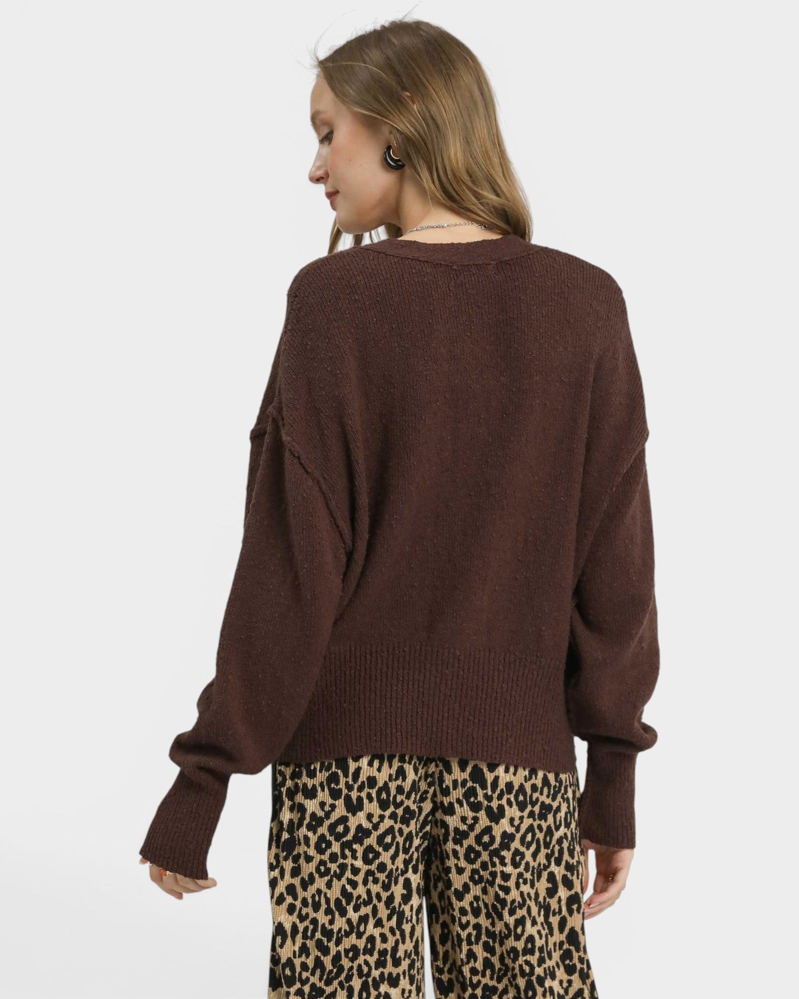 Person wearing a brown sweater and leopard print pants on a white background