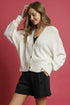 Woman wearing a white cardigan over a black top and shorts on a pink background